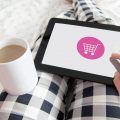 mujer en la cama, con una taza de café, haciendo compras online