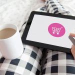 mujer en la cama, con una taza de café, haciendo compras online