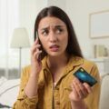 mujer hablando por teléfono angustiada con tarjeta de crédito en la mano / Shutterstock.com