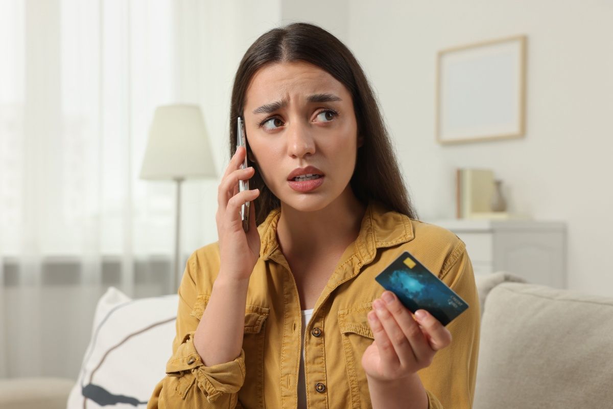 mujer hablando por teléfono angustiada con tarjeta de crédito en la mano / Shutterstock.com